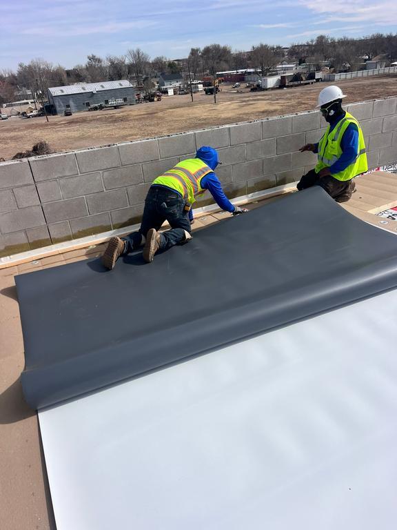 Commercial roofing crew installing a white TPO membrane on a low-slope roof in Colorado