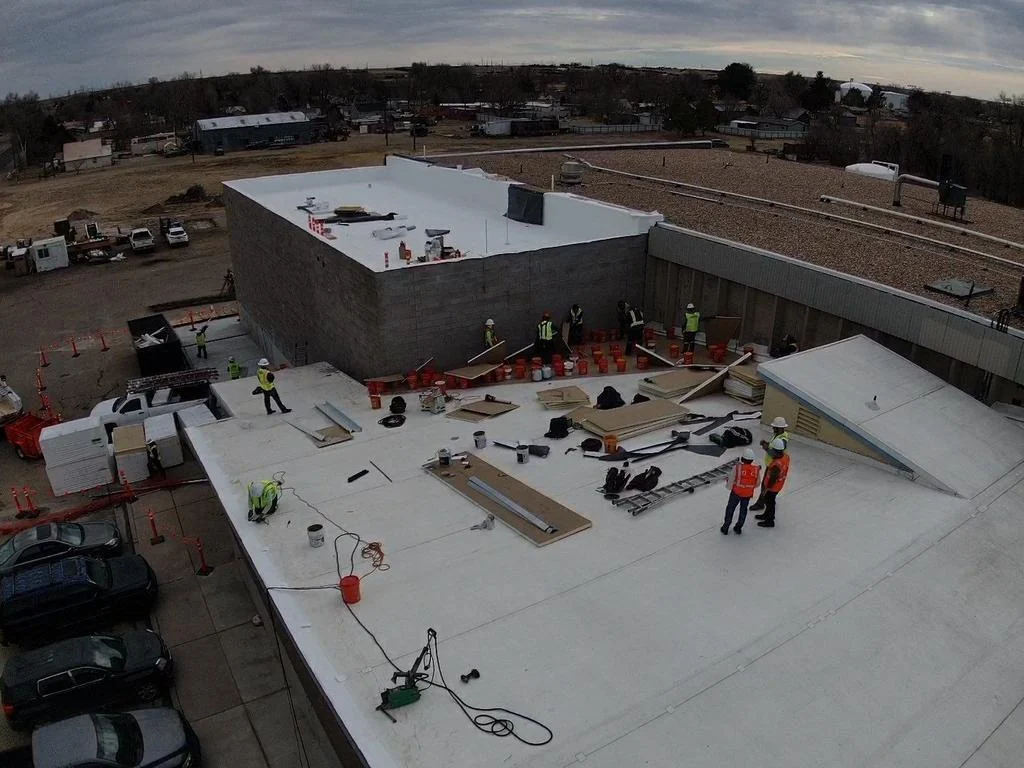 Aerial view of a commercial TPO roof installation with roofing crew and materials