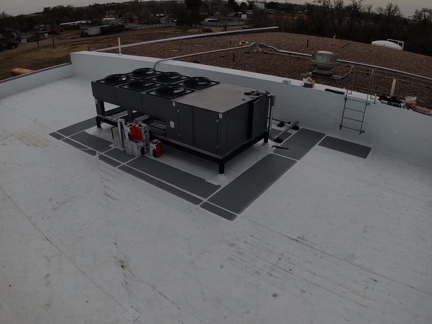 Condensing unit on a walkway pad over a white TPO roof on a commercial building