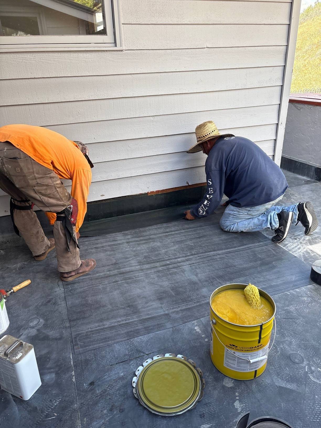 Roofing crew applying adhesive to install a fully adhered EPDM membrane