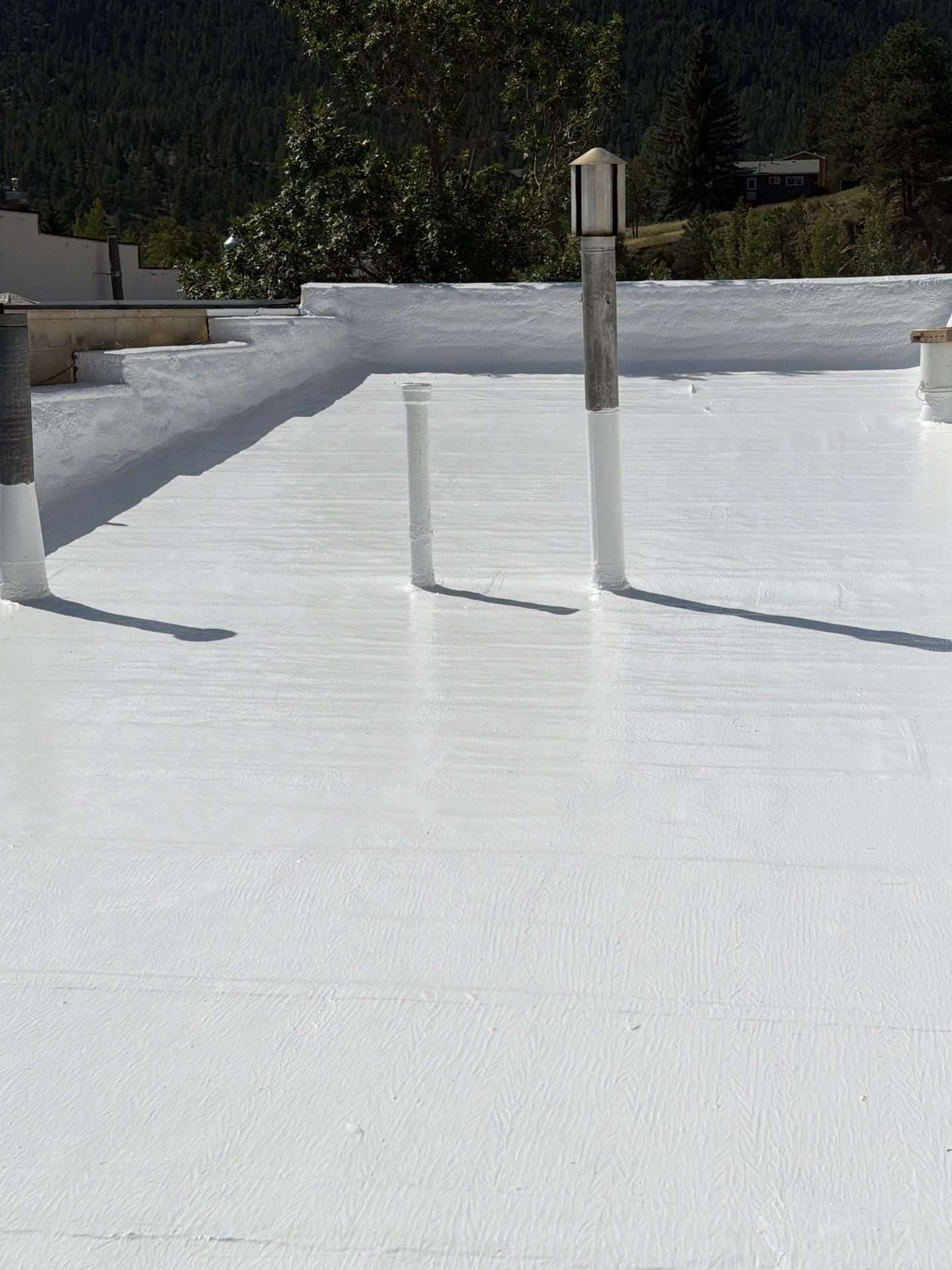Finished silicone roof coating around vent pipes and the parapet on a low-slope roof