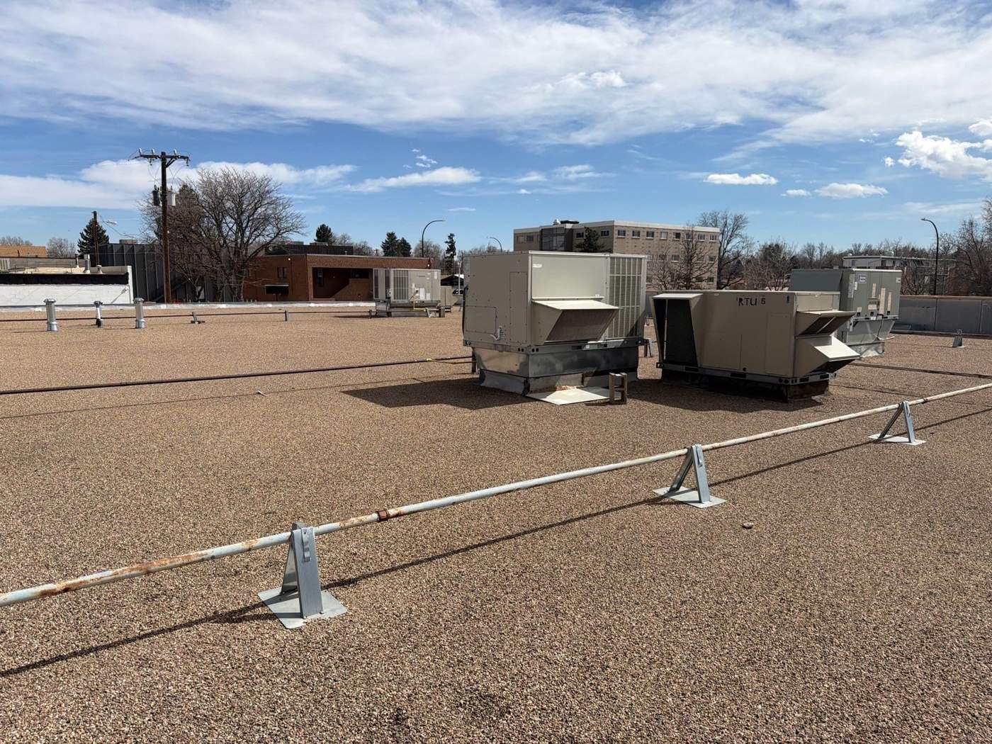Commercial flat roof with a worn gravel surface and rooftop units before a spray foam roof system