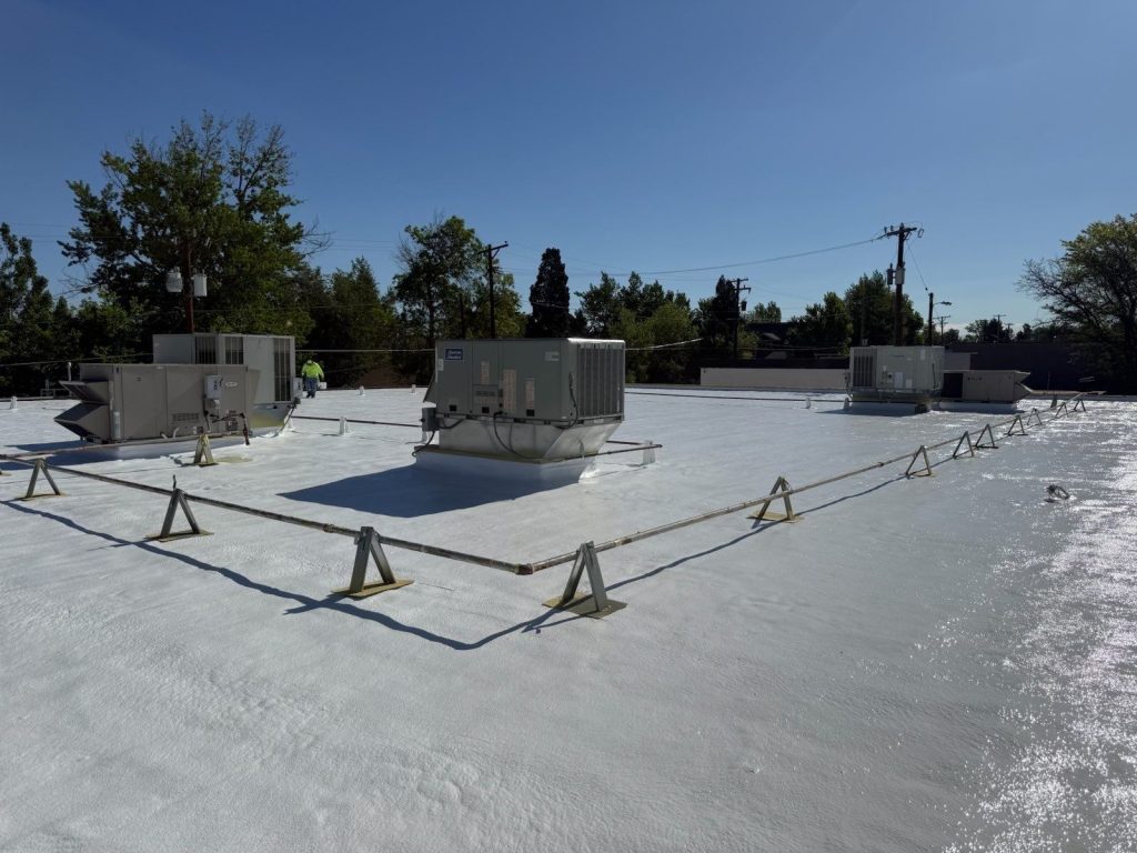 Finished white silicone coating over spray foam on a commercial roof with rooftop units
