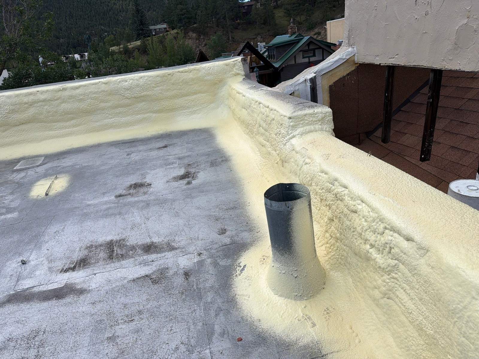 Spray foam carried up the parapet wall and around a roof penetration before the topcoat