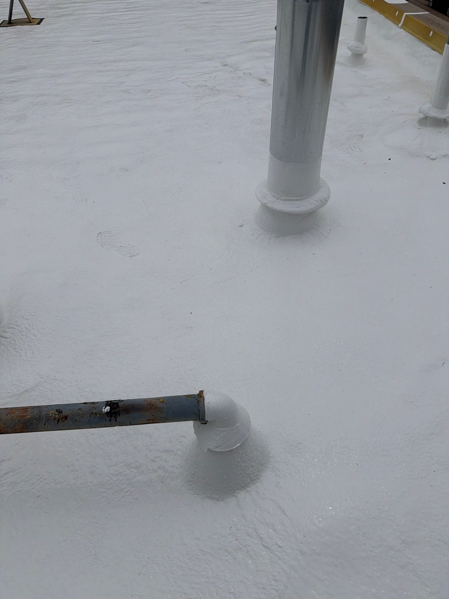 Pipe penetrations sealed with spray foam and silicone coating on a commercial roof