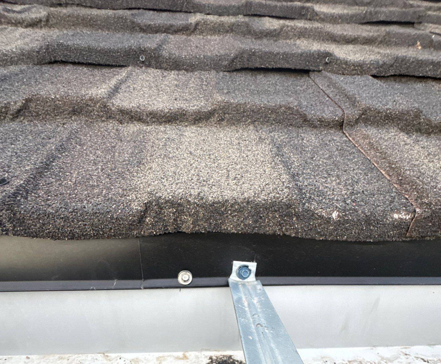 Eave edge of a stone-coated steel roof showing the panel profile above the gutter