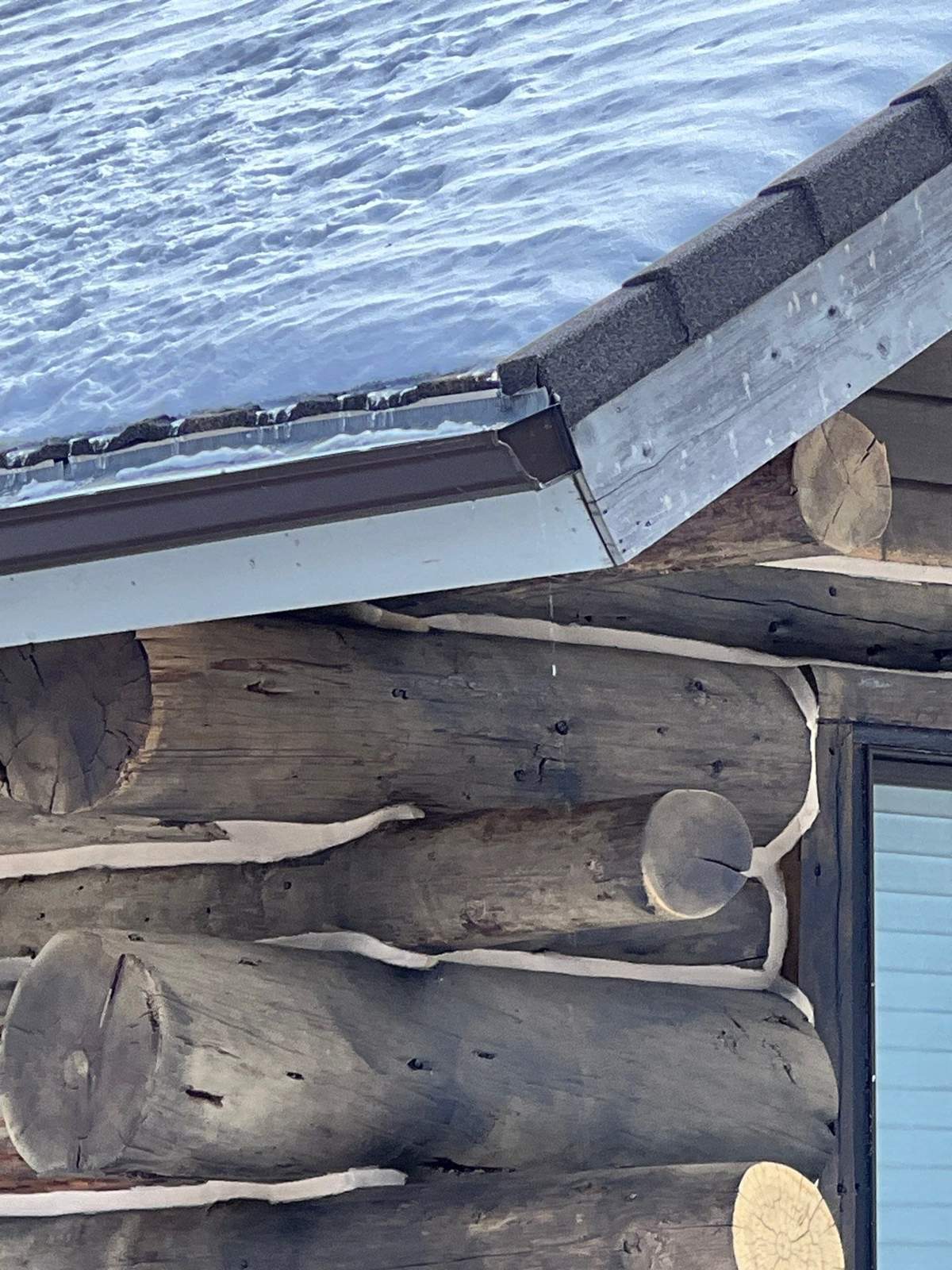 Snow on a Timberwood stone-coated steel roof edge above log corners