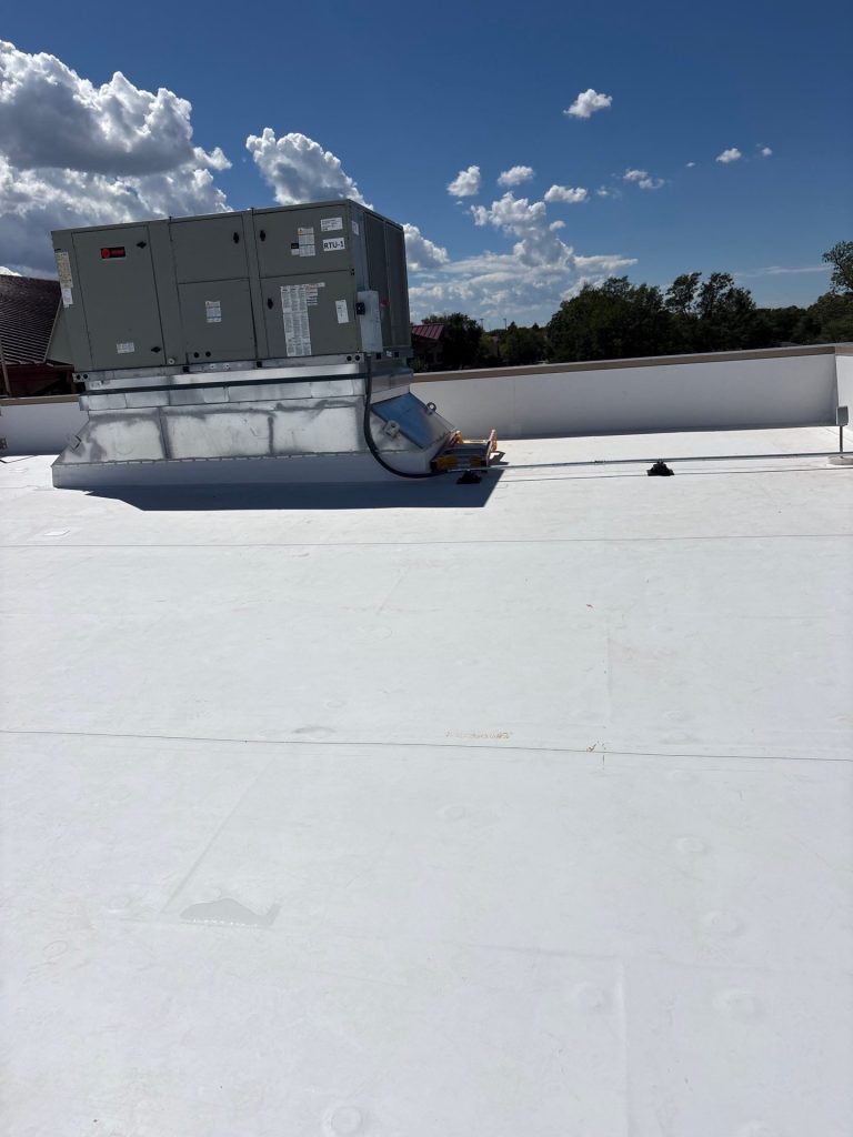 New white TPO membrane flashed around a rooftop unit on a commercial low-slope roof in Colorado.