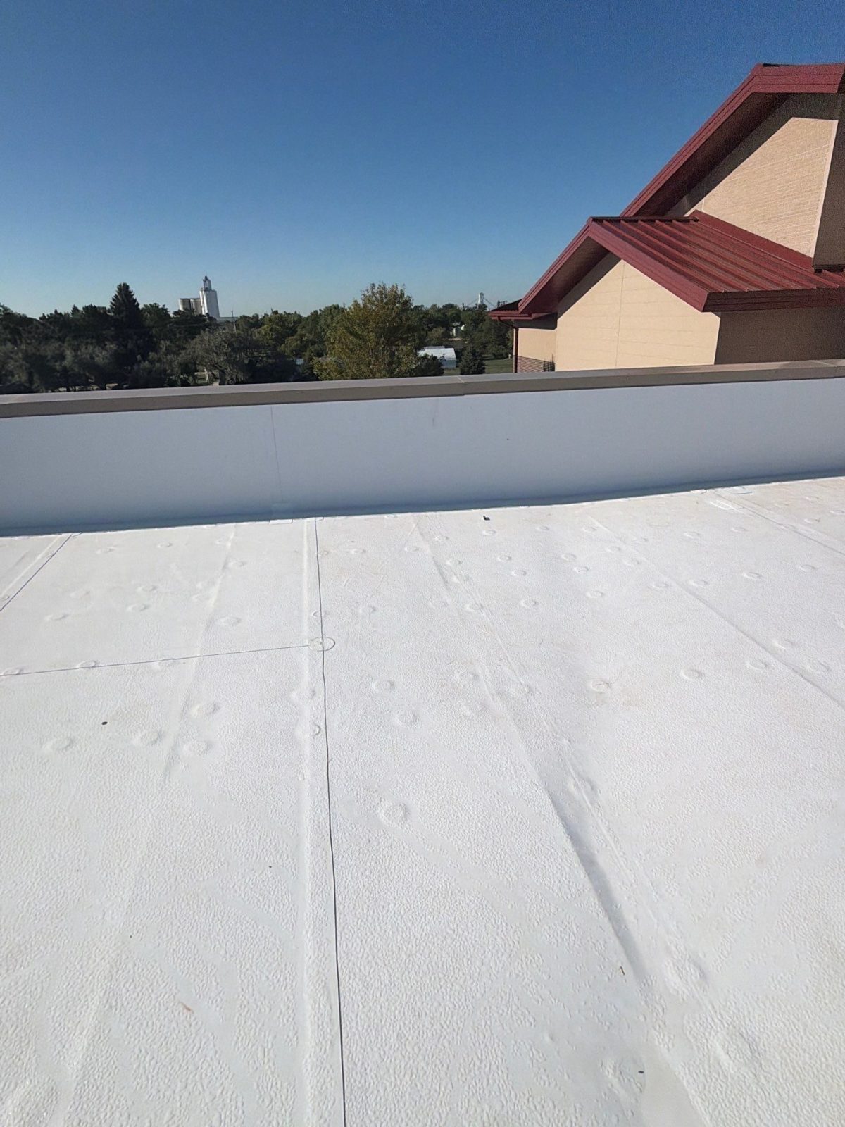 Lap seams on a new white TPO membrane running to a parapet wall on a commercial roof in Colorado.