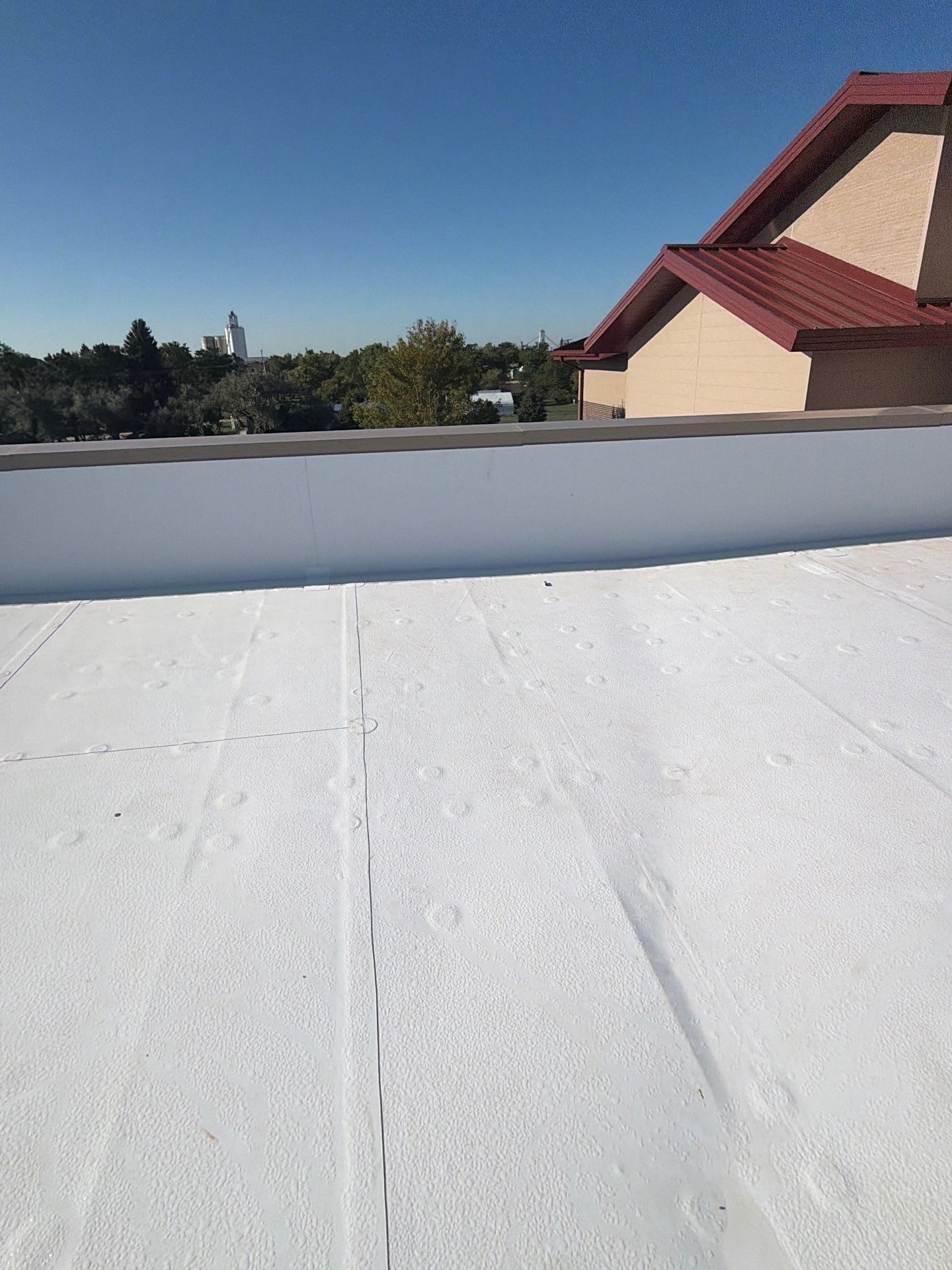 Lap seams on a new white TPO membrane running to a parapet wall on a commercial roof in Colorado.